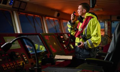 Navigator, pilot, captain part of ship crew performing daily duties with VHF radio, binoculars, logbook, standing nearby to ECDIS and radar station on board of modern ship with high quality equipment